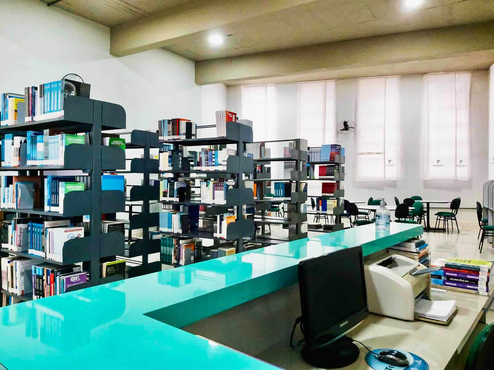 Biblioteca FAVEPORT: estantes de aço com o acervo, balcão de atendimento e mesas de estudo ao fundo